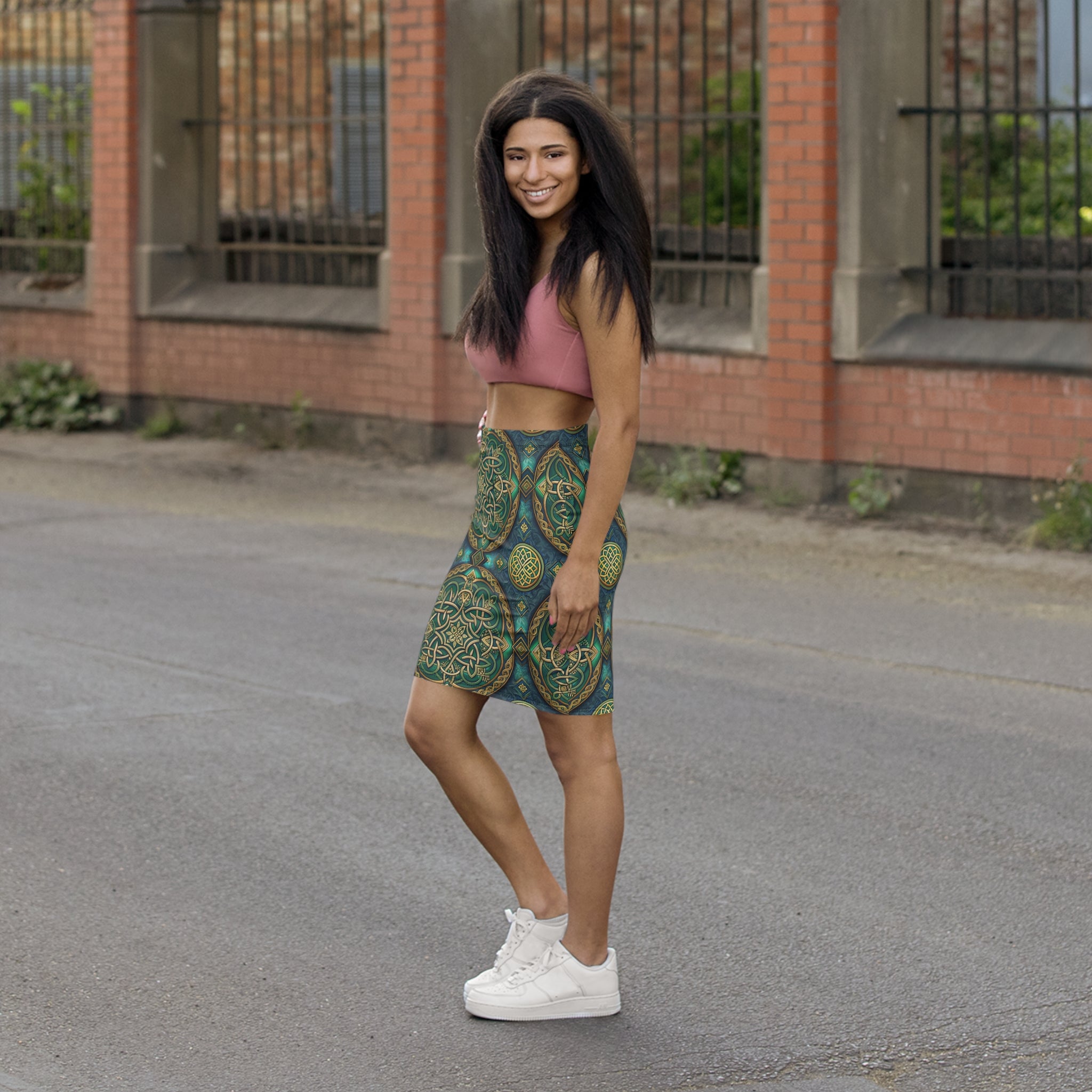 Woman wearing a patterned skirt and pink top standing on a street.