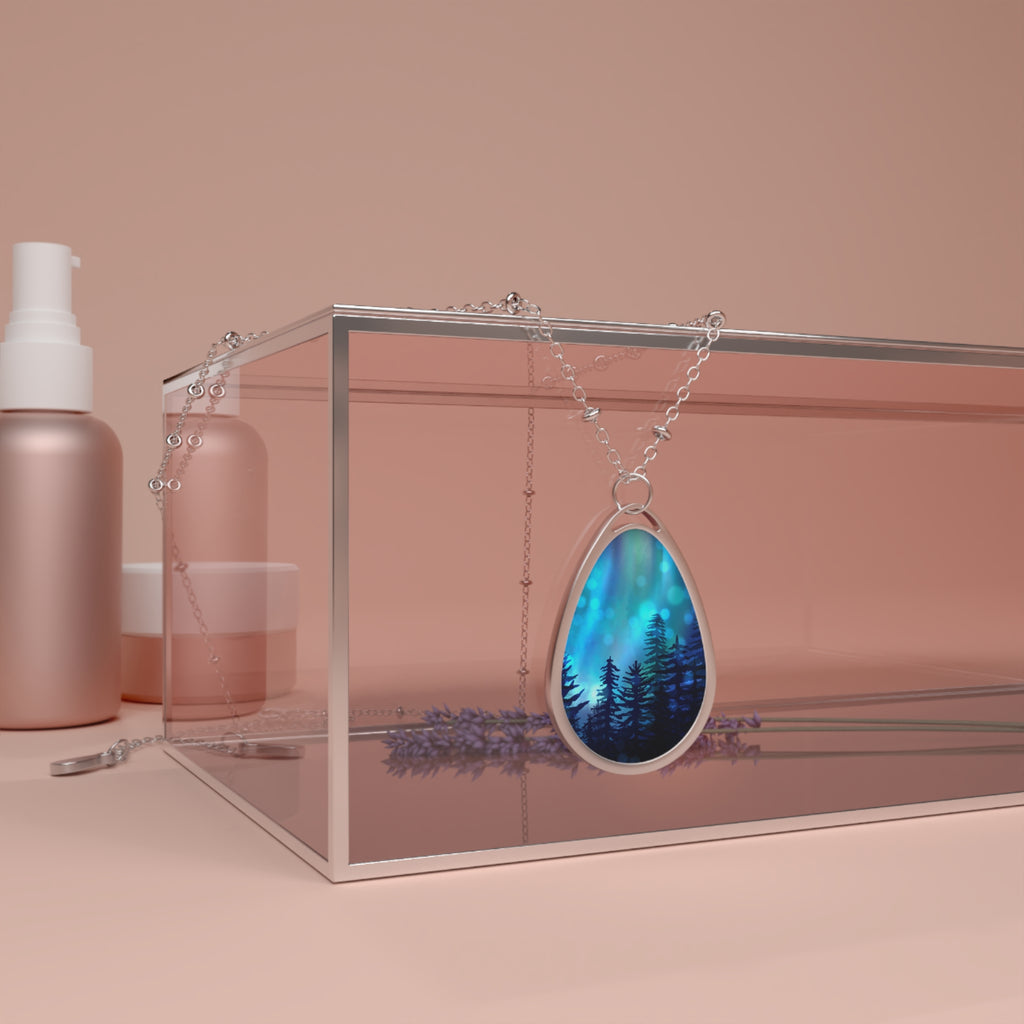 Necklace with a blue pendant featuring a forest design, displayed in a clear box on a pink background.