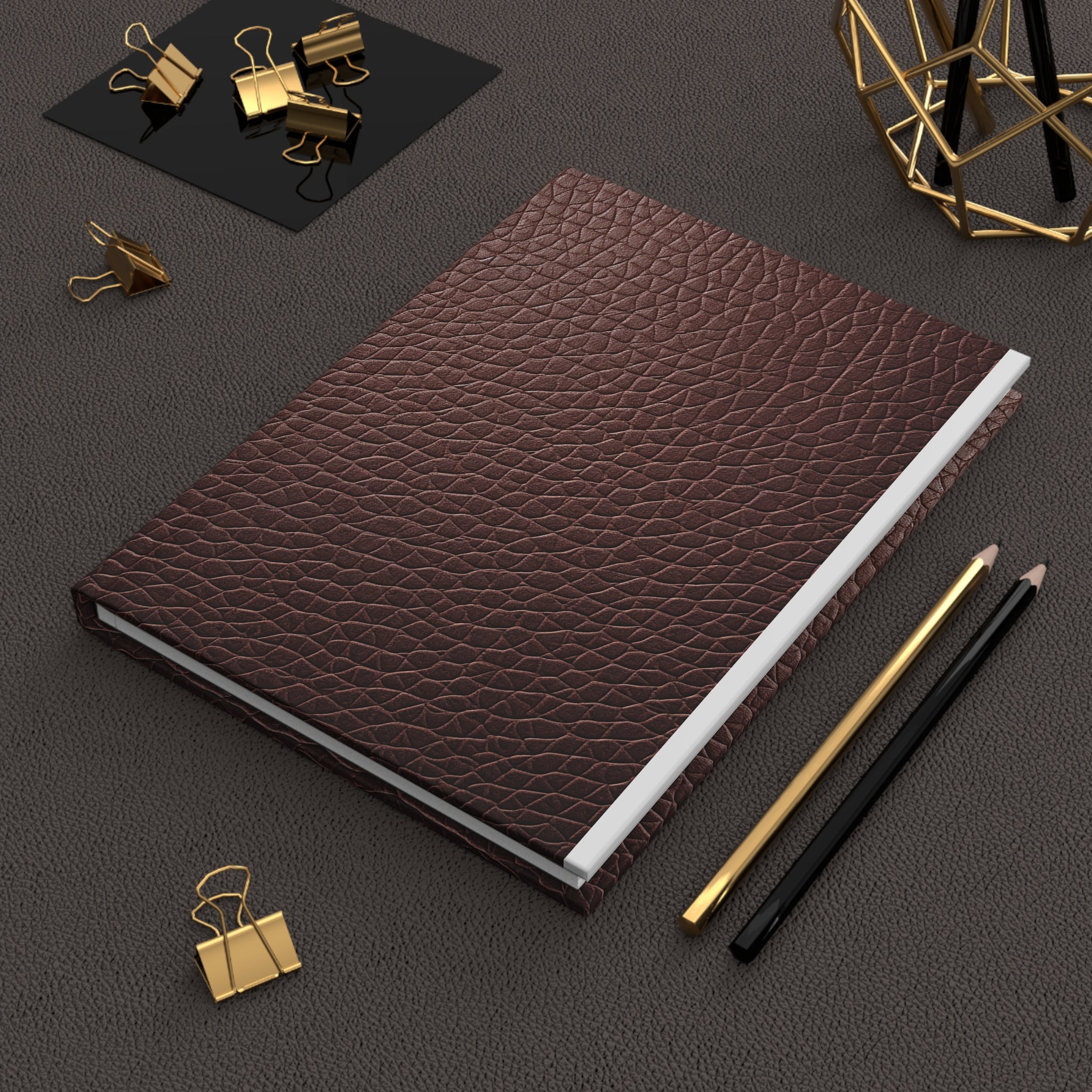 Brown faux leather notebook with gold and black office supplies on a dark surface
