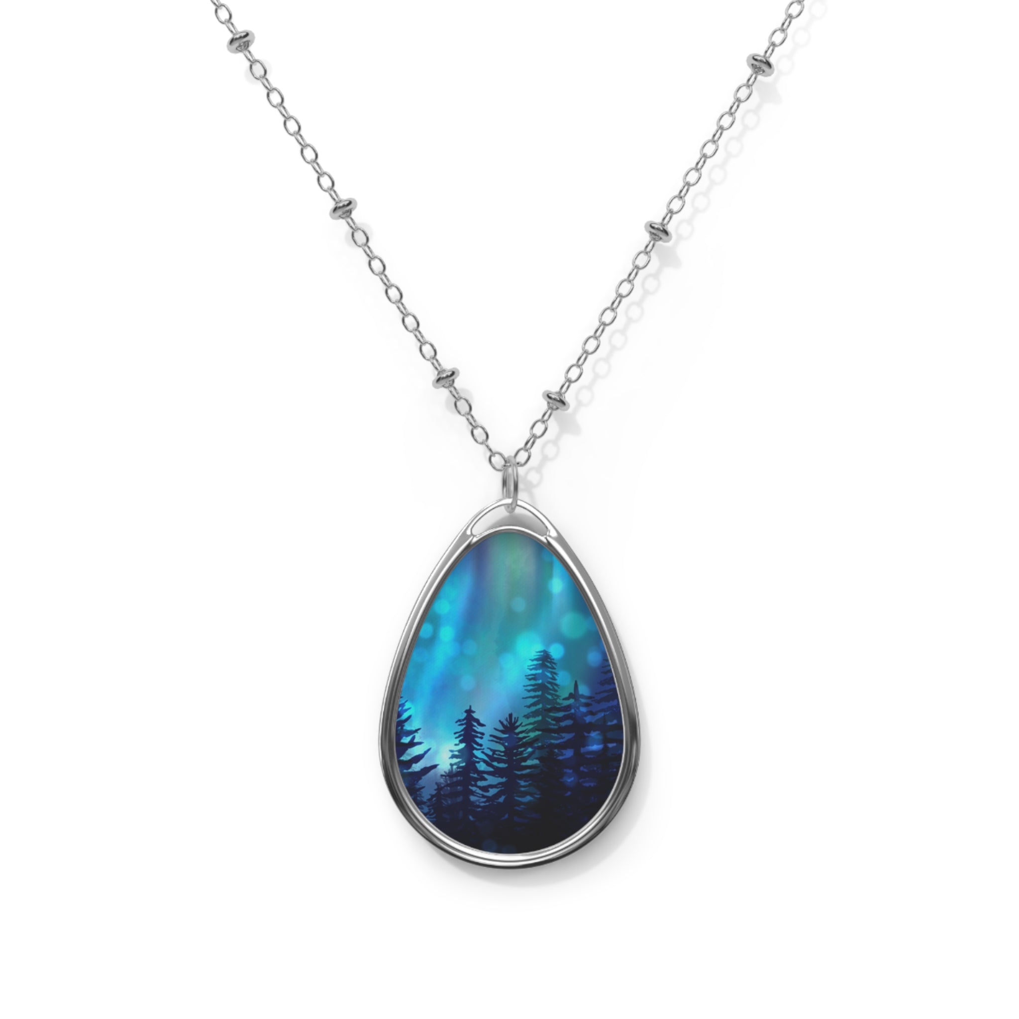 Teardrop-shaped pendant with forest design on a silver chain against a white background